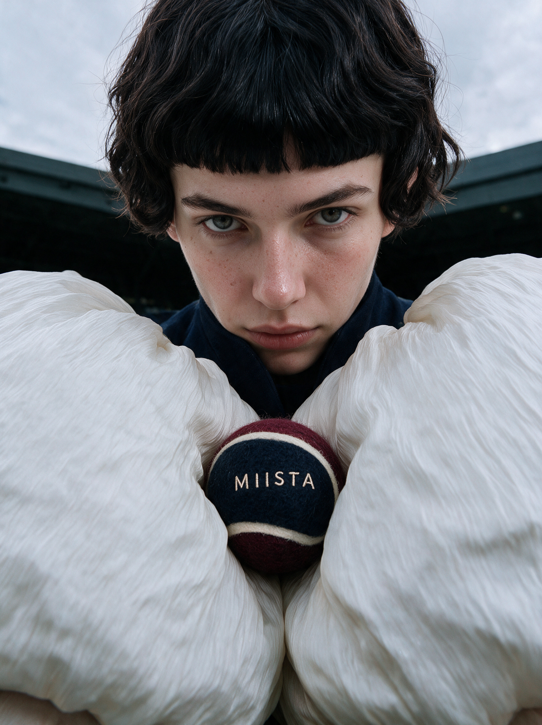 Close-up of the model holding a MIISTA tennis ball between white silk sleeves