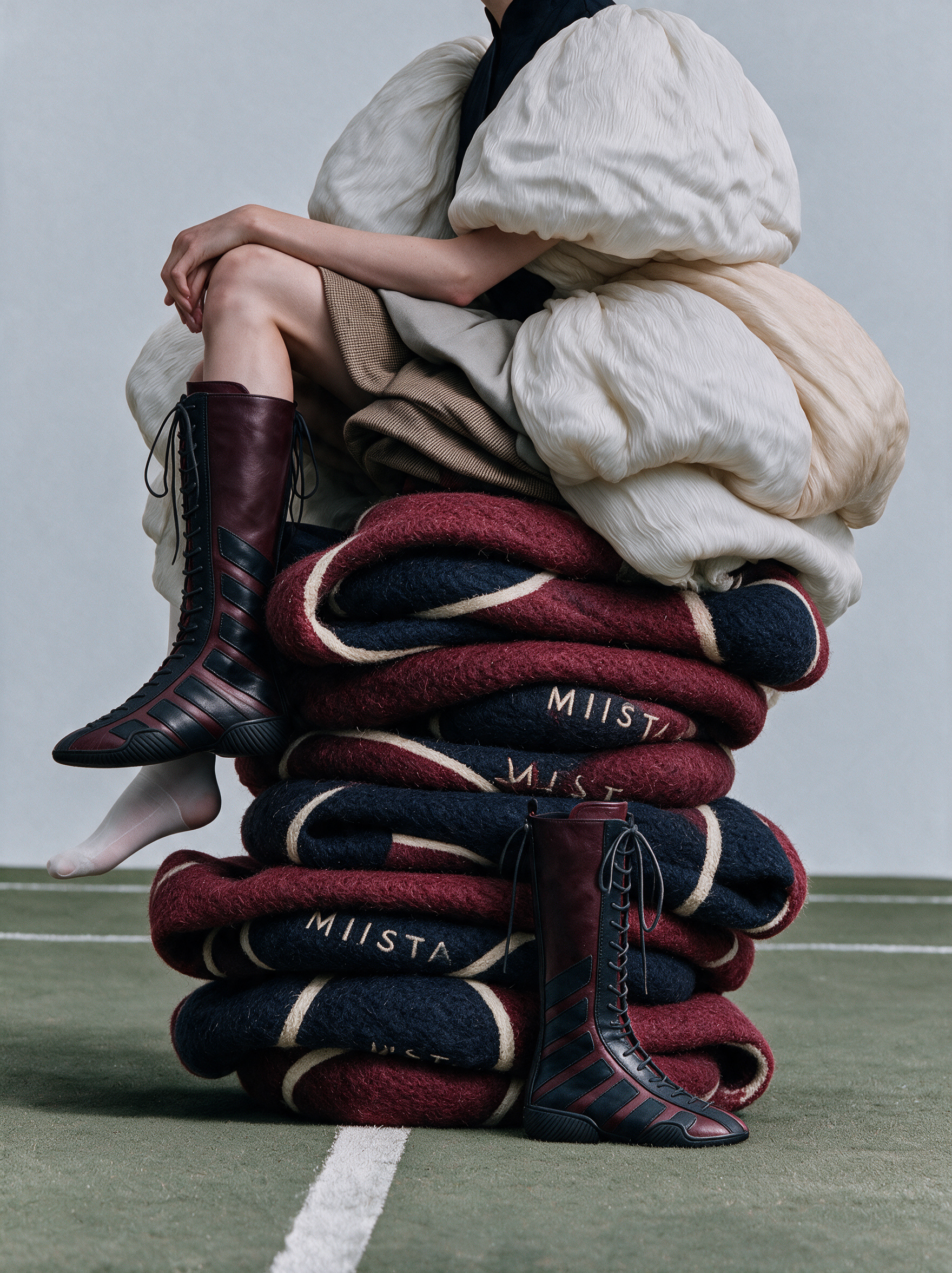 Model sitting on stacked felt blankets in MIISTA boots on a court