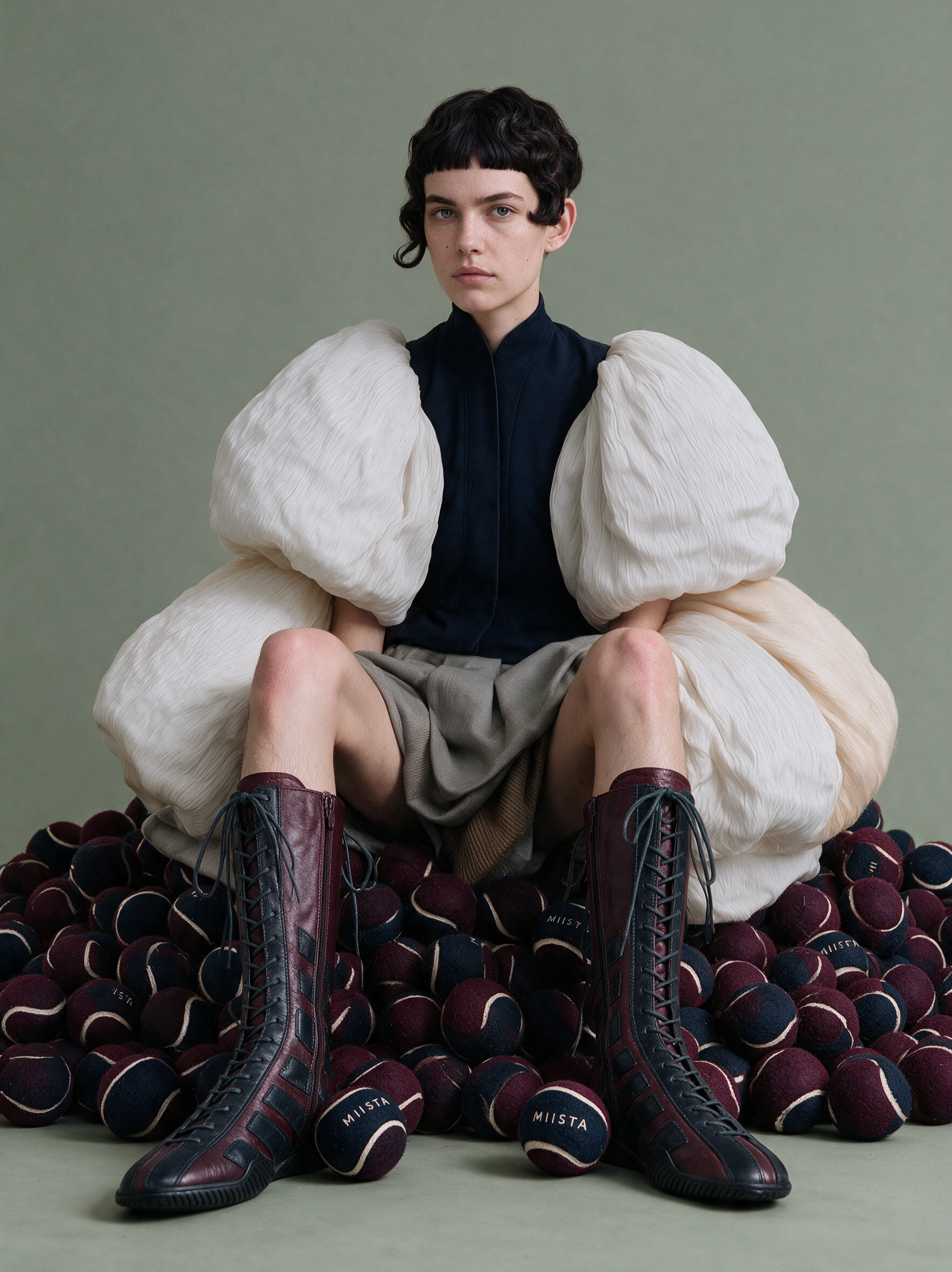 Model seated on a pile of burgundy and navy MIISTA tennis balls